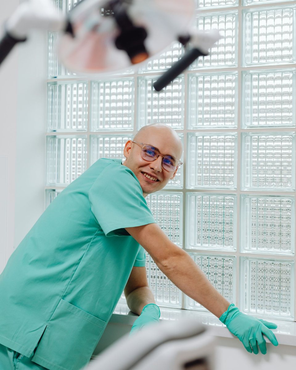 Medic stomatolog zâmbind, în uniformă verde mentă, în cabinet